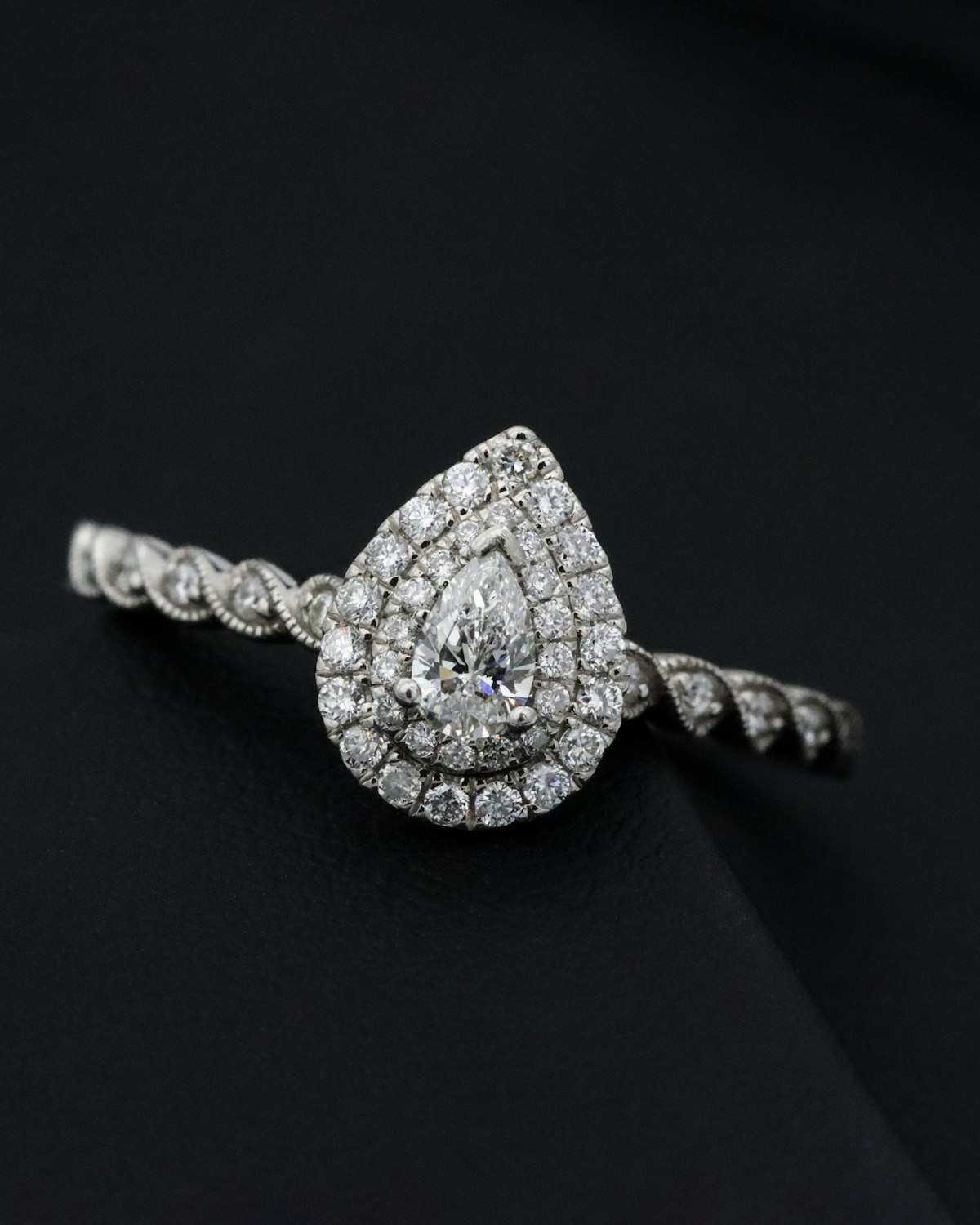 Pear-cut diamond ring with a double diamond halo setting, on a dark surface